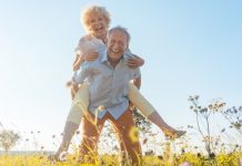 Happy senior man laughing while carrying his partner on his back in the countryside