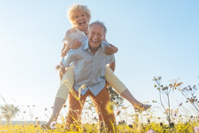 Happy senior man laughing while carrying his partner on his back in the countryside