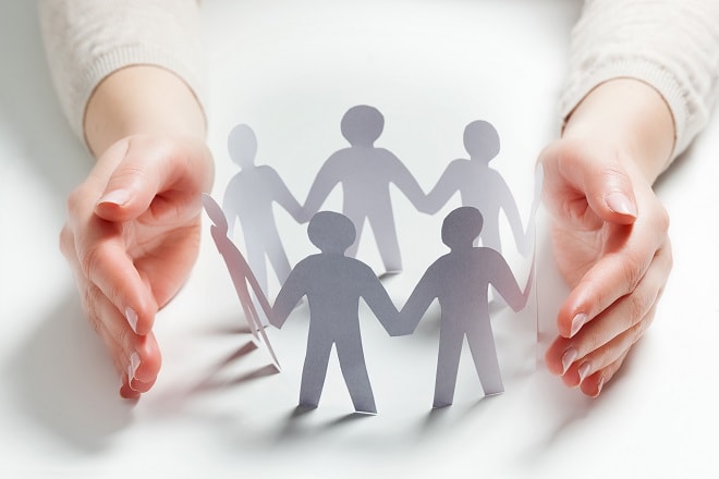 Paper People Surrounded By Hands In Gesture Of Protection. Concept Of Insurance