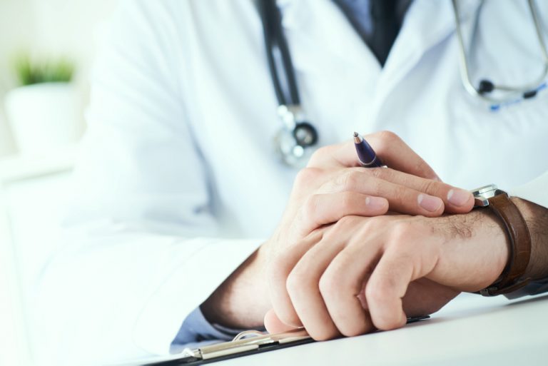 Man Doctor With Stethoscope Looking At Wrist Watch. Doctor In White Uniform At Office Background Waiting For Patients. Time To Visit Therapist.