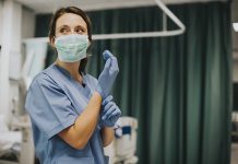 Female Nurse With A Mask Putting On Gloves