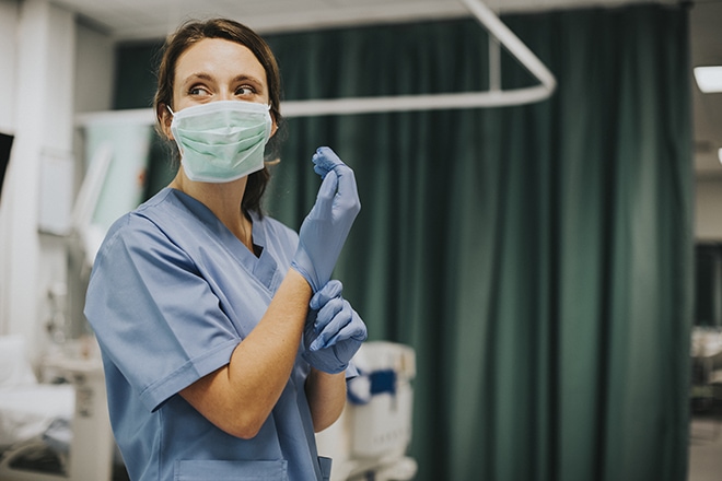 Female Nurse With A Mask Putting On Gloves