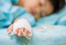 Closeup Kid Hand Sleeps On A Bed In Hospital With Saline Intravenous, Selective Focus.