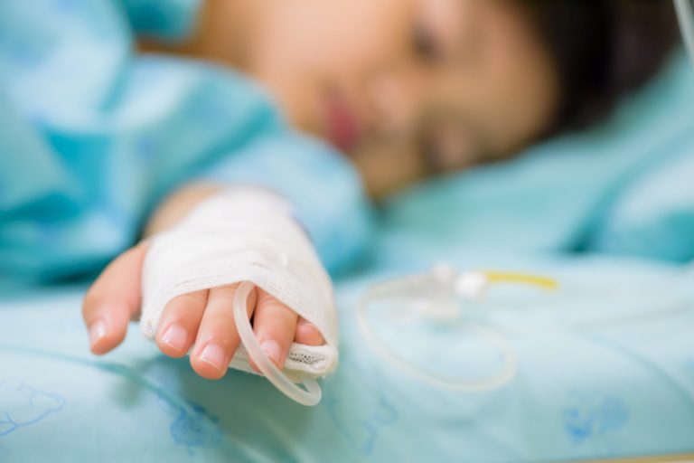 Closeup Kid Hand Sleeps On A Bed In Hospital With Saline Intravenous, Selective Focus.