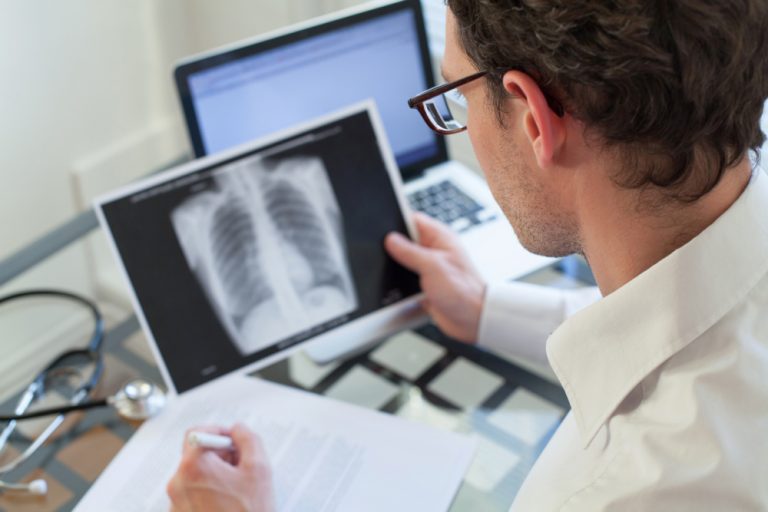 Doctor Looking At X Ray Of Lungs And Writing Diagnosis