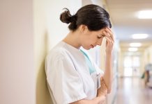 Upset Female Nurse Standing In Hospital Corridor