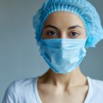 Portrait of a female doctor or nurse wearing medical cap and face mask looking at the camera.