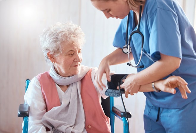Disability, monitor and old woman with a nurse for blood pressure check in a medical healthcare hospital. Wheelchair, doctor and caregiver helping a sick elderly person in a nursing home