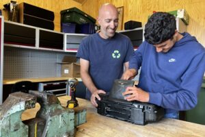 In de demontageloods van de ecostraat halen begeleider Patrick en deelnemer Dani een oude radio uit elkaar.